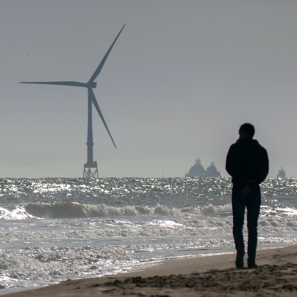 Man walking along beach with sea based wind turbine in the background